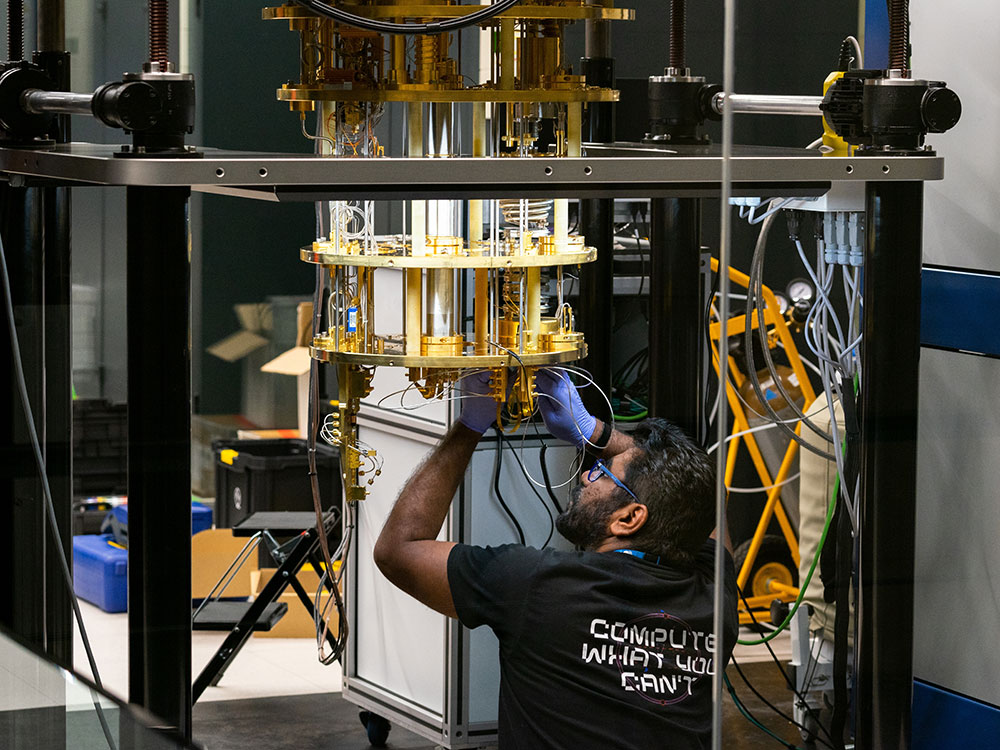 Photograph of a person in glasses and gloves manipulating a large piece of equipment that consists of tubes of various materials and sizes and a large metal frame. 