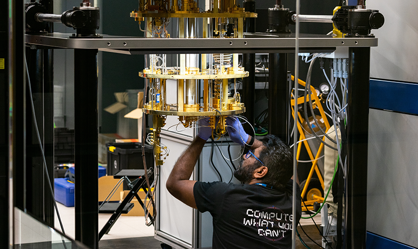 Photograph of a person in glasses and gloves manipulating a large piece of equipment that consists of tubes of various materials and sizes and a large metal frame. 