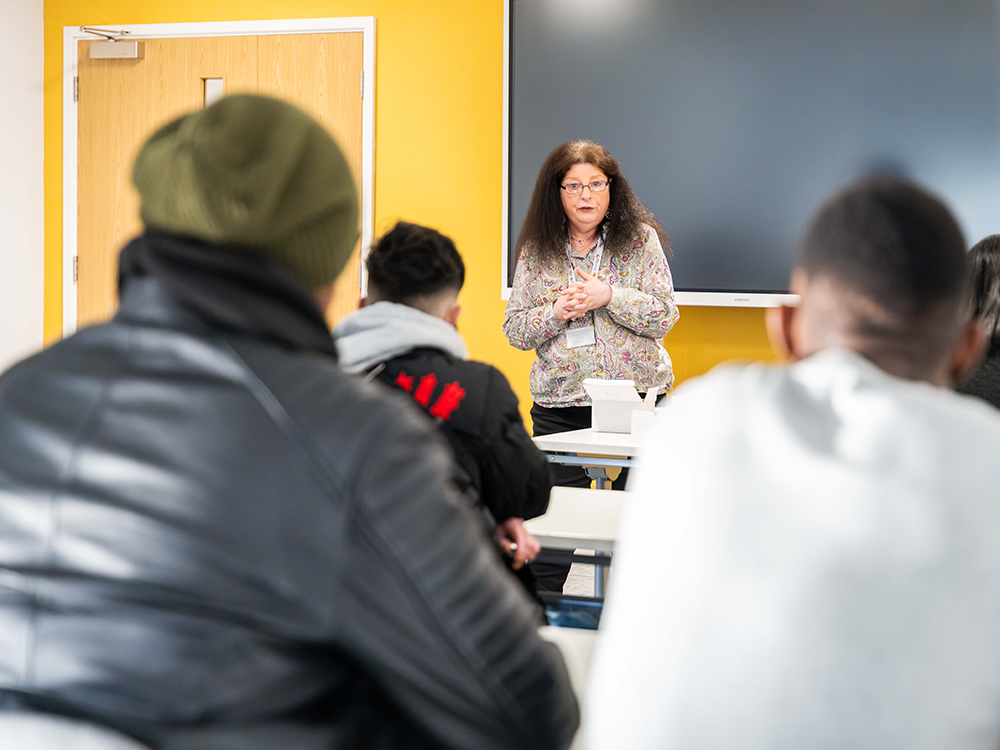 photo of a person speaking at the front of a classroom full of students