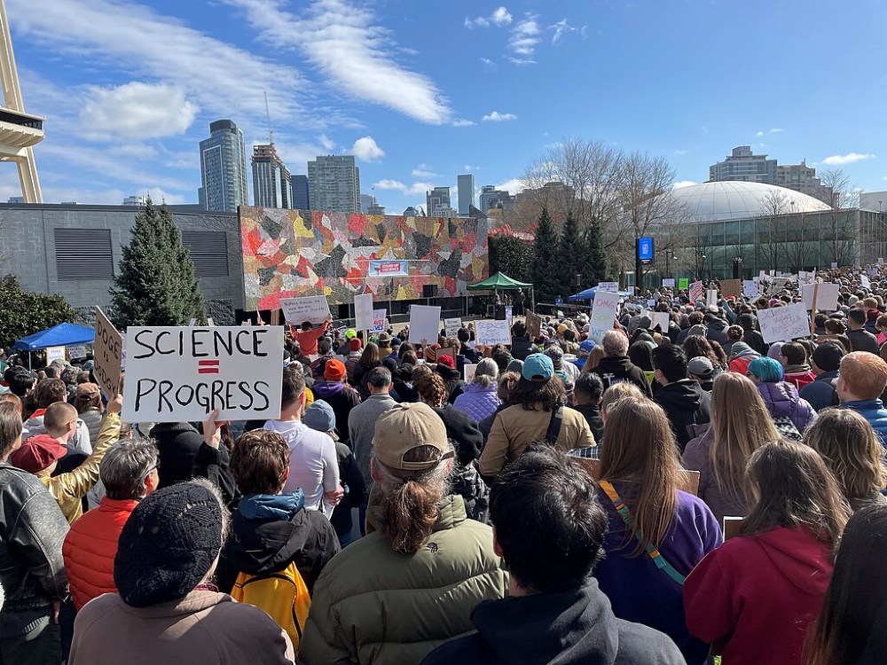 A photograph of a crowd of people at the Stand Up For Science protest in Seattle, Washington on 07 March 2025. Many people are holding signs, one of which says 