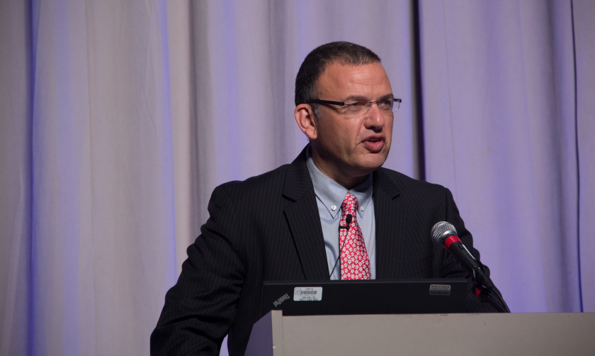 Matti Shem Tov standing at a podium in front of a curtain 