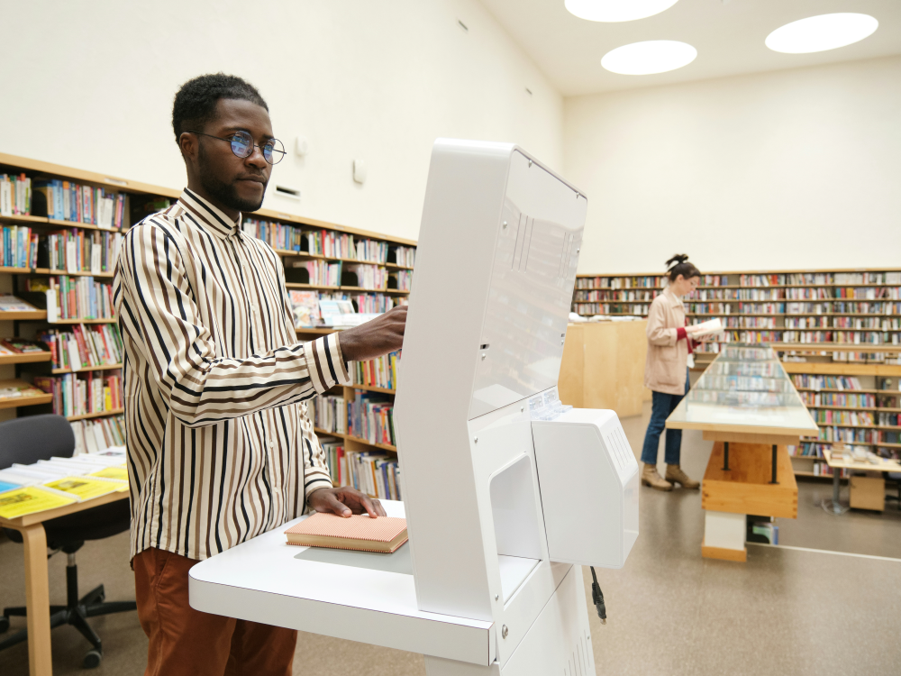 A man uses a touch screen machine to scan a book in a library. 