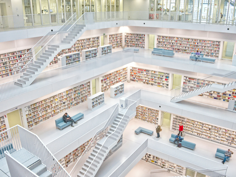 The interior of a library building with several floors lined with bookshelves, with exposed staircases, surrounding an open area