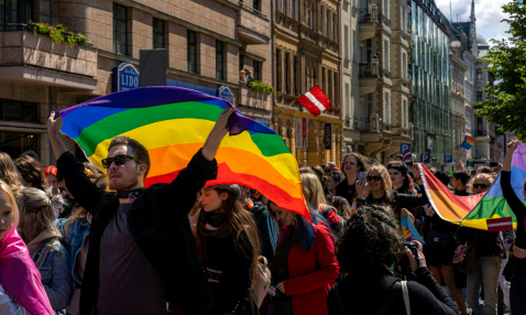 A group of people filling a street, displaying rainbow flags and Latvian flags.