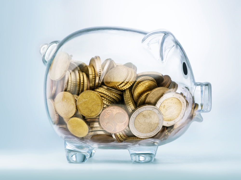 A transparent piggy bank filled with coins of various currencies. 