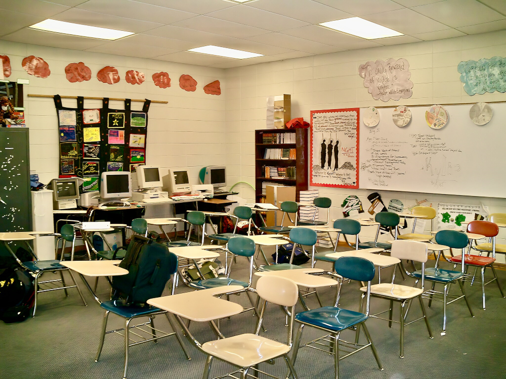 Rows of desks in a high school classroom with a white board and computers against one wall