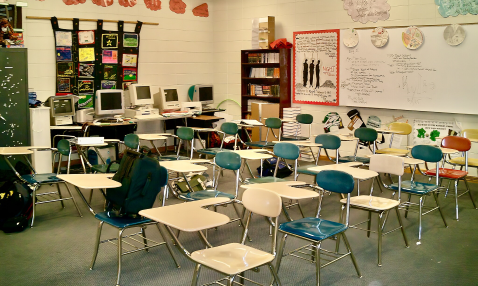 Rows of desks in a high school classroom with a white board and computers against one wall