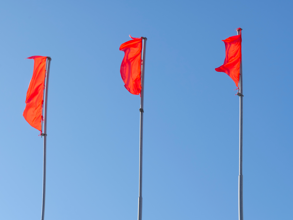 Three red flags on flag poles, waving against a blue sky 