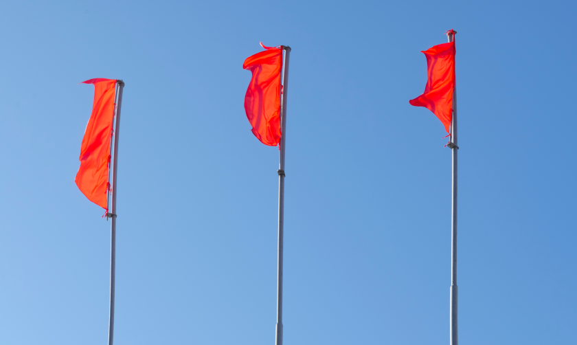 Three red flags on flag poles, waving against a blue sky 