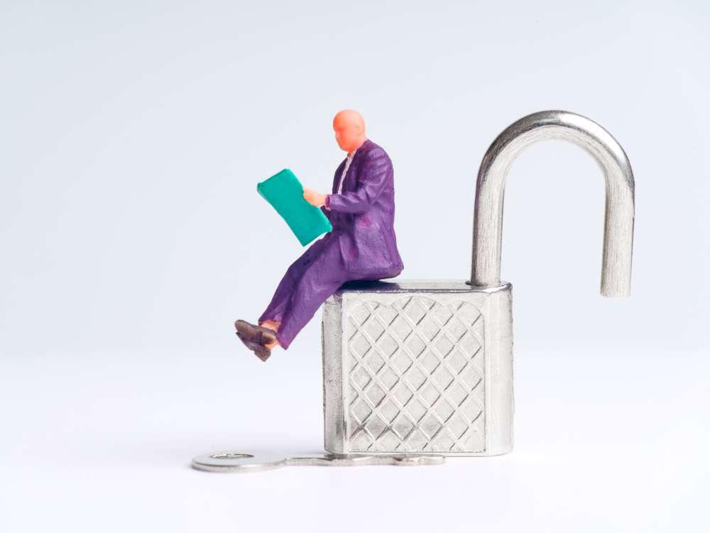 A figurine sits reading atop an open padlock.