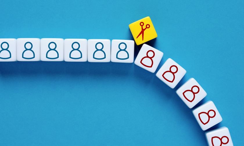 A row of cubes with outlines of people on them, divided by a cube with a pair of scissors on it, after which the people are red instead of blue and the row slants downward, as if they cubes are falling. 